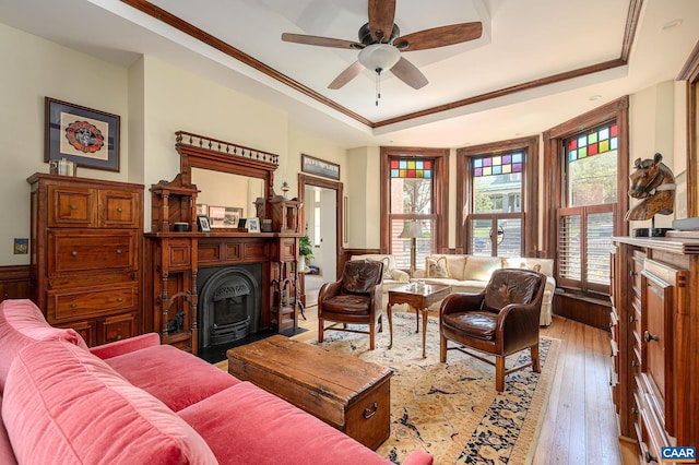 living room featuring ceiling fan, a raised ceiling, a wood stove, ornamental molding, and hardwood / wood-style flooring