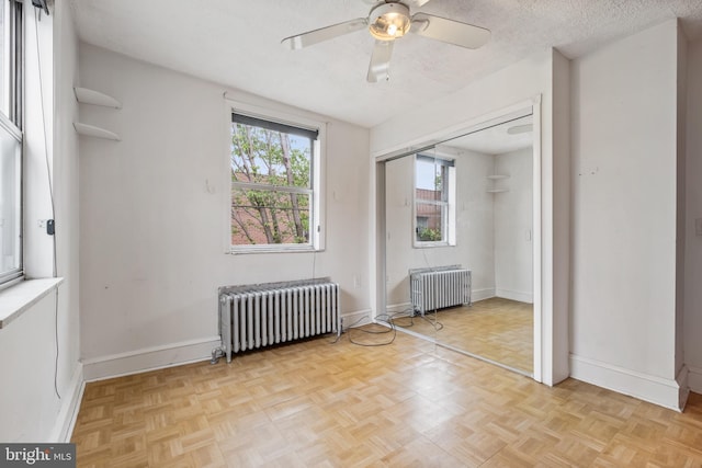 unfurnished bedroom with ceiling fan, a textured ceiling, radiator, and light parquet floors