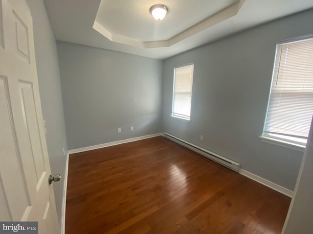 empty room with dark wood-type flooring, a baseboard heating unit, and a raised ceiling