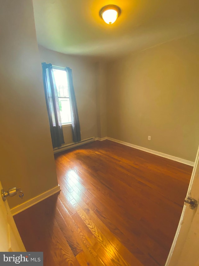 empty room featuring baseboard heating and dark wood-type flooring