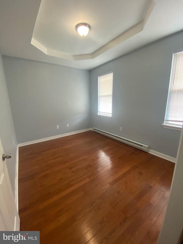 empty room with dark hardwood / wood-style flooring, a baseboard radiator, and a wealth of natural light