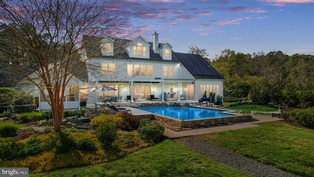 pool at dusk featuring a patio area and a lawn