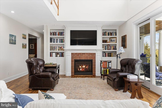 living room with hardwood / wood-style flooring, built in shelves, and a brick fireplace