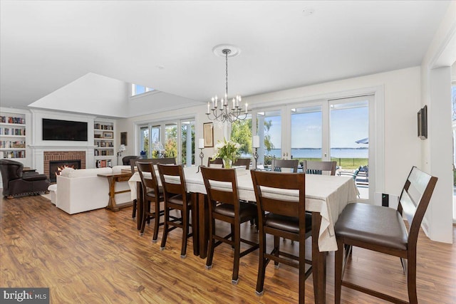 dining area with a brick fireplace, a water view, a notable chandelier, wood-type flooring, and built in shelves