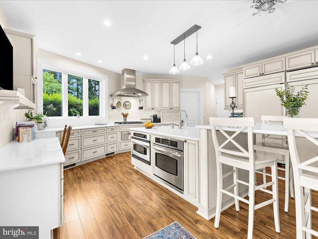 kitchen featuring a center island with sink, stainless steel gas stovetop, hardwood / wood-style floors, wall chimney exhaust hood, and pendant lighting