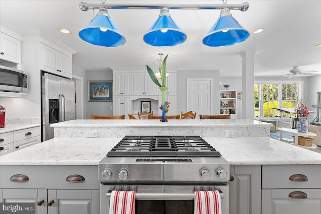 kitchen featuring a kitchen island, appliances with stainless steel finishes, white cabinets, light stone counters, and ceiling fan