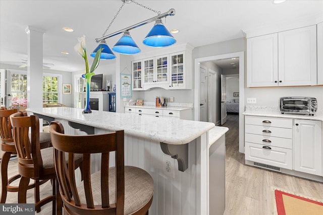 kitchen with light stone counters, light hardwood / wood-style flooring, a kitchen breakfast bar, hanging light fixtures, and white cabinets