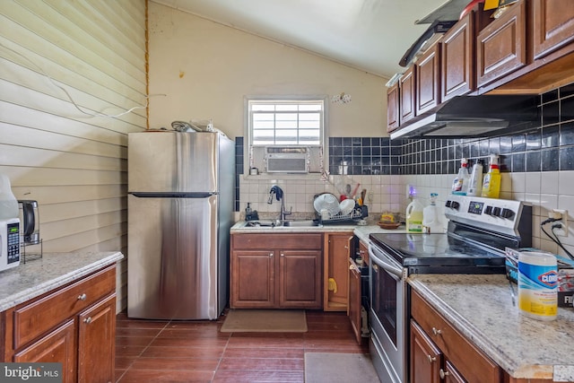 kitchen featuring tasteful backsplash, wooden walls, appliances with stainless steel finishes, sink, and lofted ceiling