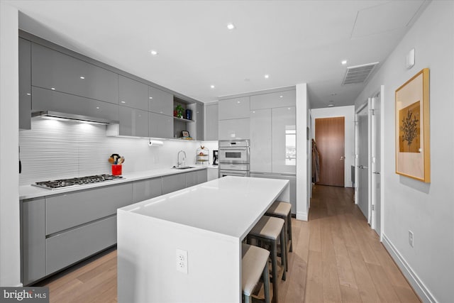 kitchen with light hardwood / wood-style flooring, backsplash, a center island, gray cabinets, and appliances with stainless steel finishes