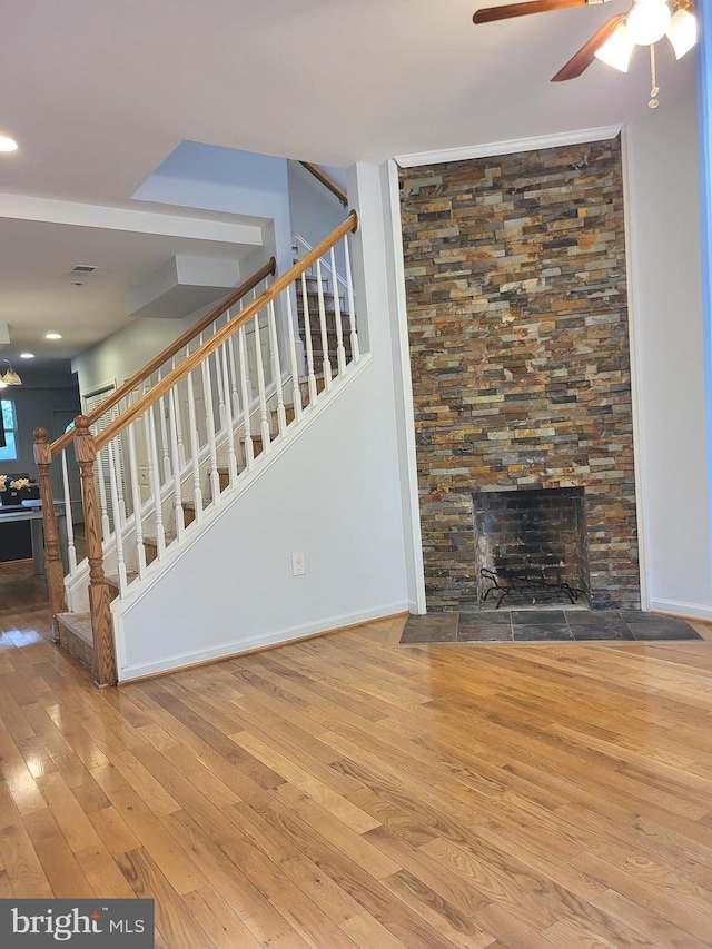 unfurnished living room featuring wood-type flooring, ceiling fan, and a stone fireplace