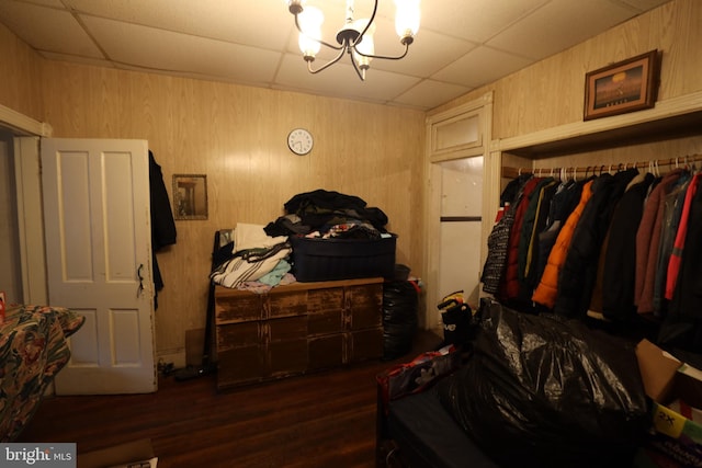 bedroom with wooden walls, a drop ceiling, dark wood-type flooring, and a notable chandelier