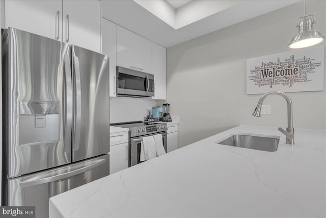 kitchen with stainless steel appliances, sink, decorative light fixtures, light stone countertops, and white cabinetry