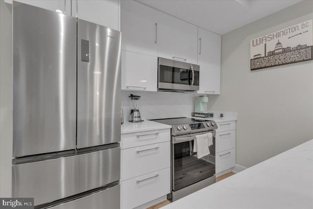 kitchen with backsplash, white cabinets, appliances with stainless steel finishes, light hardwood / wood-style floors, and light stone counters