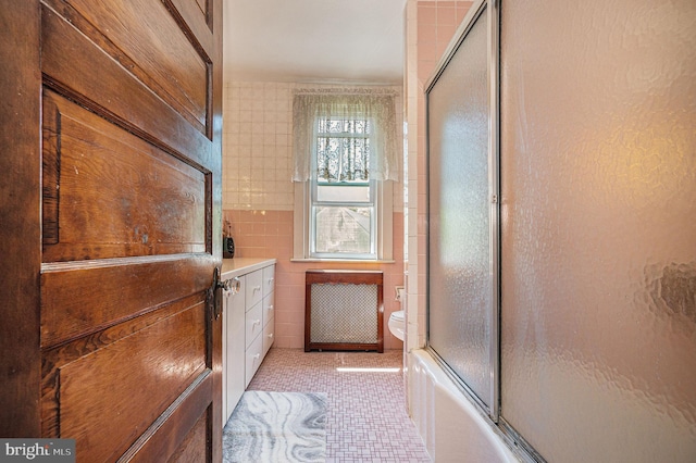 full bathroom with radiator, tile patterned floors, shower / bath combination with glass door, vanity, and tile walls