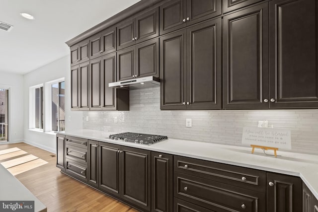 kitchen with dark brown cabinets, stainless steel gas stovetop, tasteful backsplash, and light hardwood / wood-style flooring