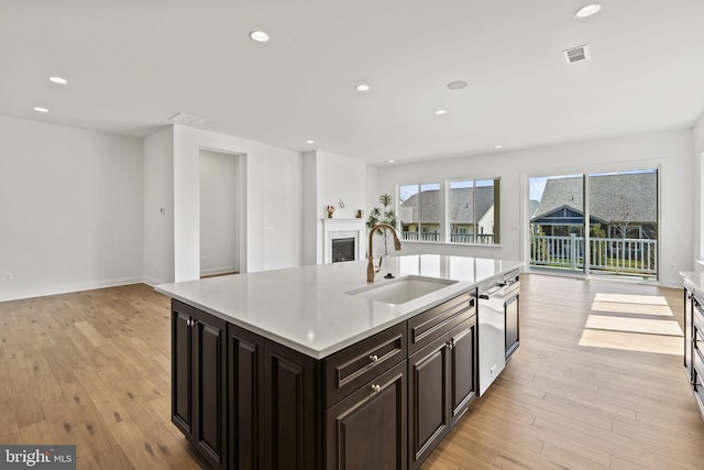 kitchen featuring an island with sink, sink, light wood-type flooring, and dark brown cabinets