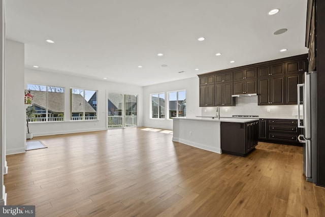 kitchen with a kitchen island with sink, stainless steel refrigerator, light wood-type flooring, and dark brown cabinets