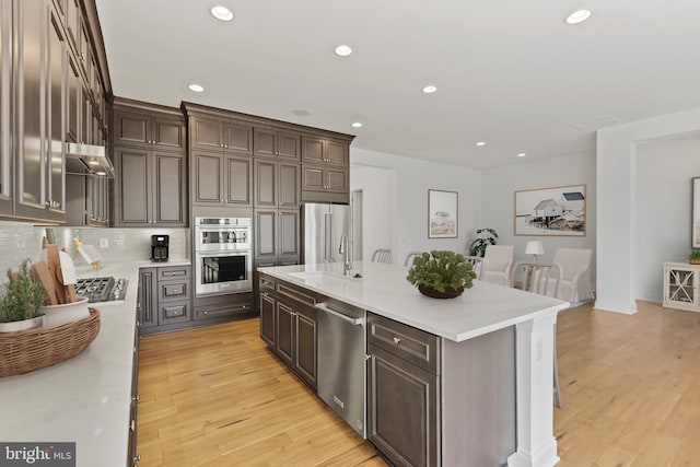 kitchen with light hardwood / wood-style floors, a kitchen island, stainless steel appliances, backsplash, and sink