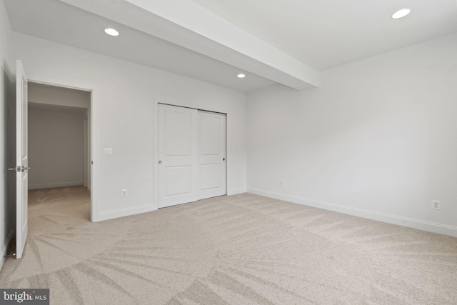 unfurnished bedroom with beamed ceiling, a closet, and carpet floors