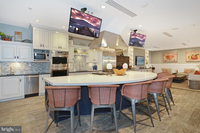 kitchen featuring backsplash, island exhaust hood, built in appliances, a large island, and a breakfast bar