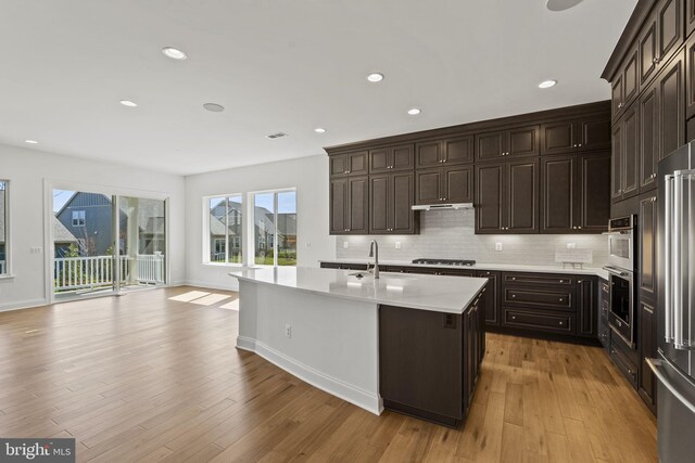 kitchen featuring light hardwood / wood-style floors, tasteful backsplash, gas stovetop, and a center island with sink