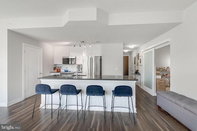 kitchen featuring white cabinets, an island with sink, stainless steel refrigerator, and dark wood-type flooring