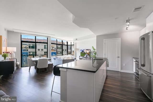 kitchen with floor to ceiling windows, stainless steel fridge, an island with sink, and dark wood-type flooring