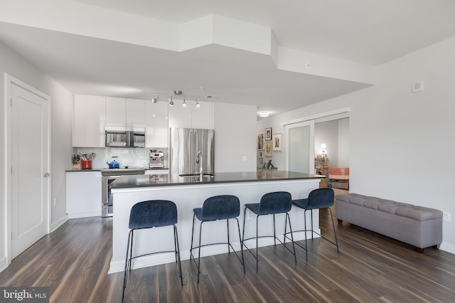 kitchen featuring white cabinetry, tasteful backsplash, dark hardwood / wood-style flooring, an island with sink, and appliances with stainless steel finishes