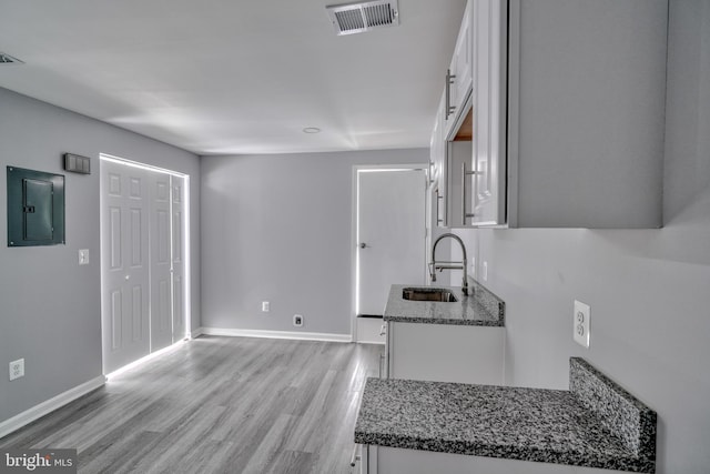 kitchen with light wood-type flooring, sink, dark stone countertops, electric panel, and white cabinetry