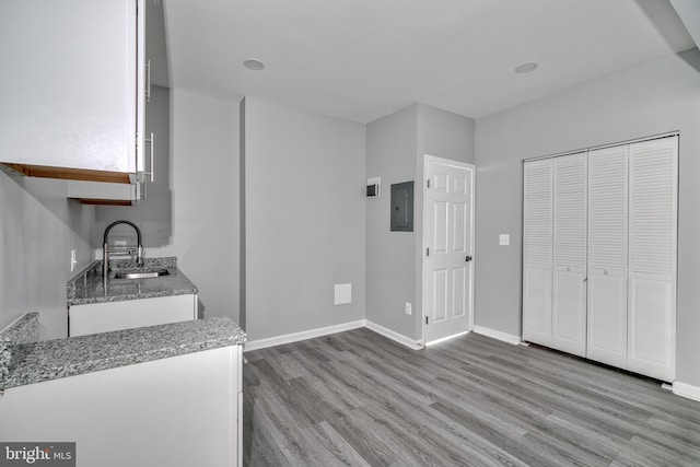 kitchen featuring electric panel, white cabinetry, sink, and light hardwood / wood-style flooring