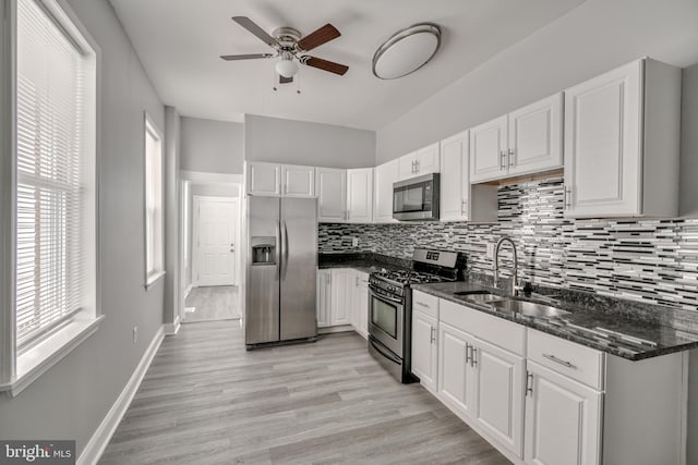 kitchen with white cabinetry, sink, stainless steel appliances, light hardwood / wood-style flooring, and dark stone countertops