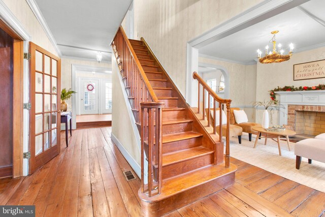 stairs featuring an inviting chandelier, wood-type flooring, crown molding, and french doors