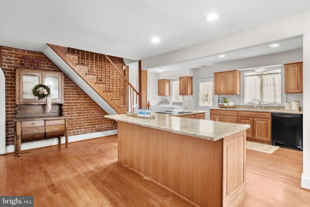 1791 Warrenton Rd, Fredericksburg, VA 22406 - kitchen with black dishwasher, light wood-type flooring, light stone counters, brick wall, and washing machine and clothes dryer