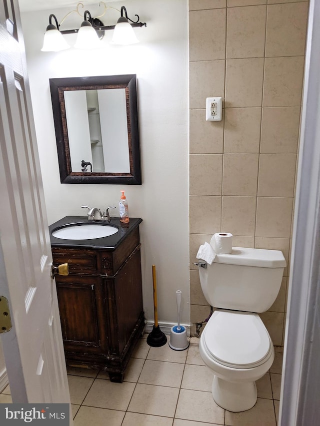 half bath featuring tile walls, toilet, vanity, baseboards, and tile patterned floors