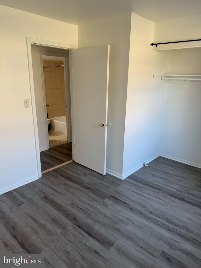 unfurnished bedroom featuring a closet, dark wood-style flooring, and baseboards