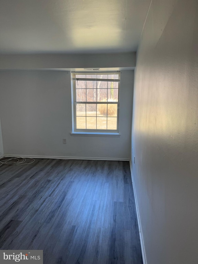 spare room featuring dark wood-type flooring and baseboards