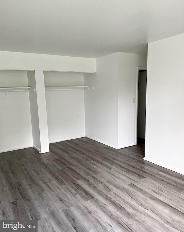 unfurnished bedroom featuring baseboards, wood finished floors, and multiple closets