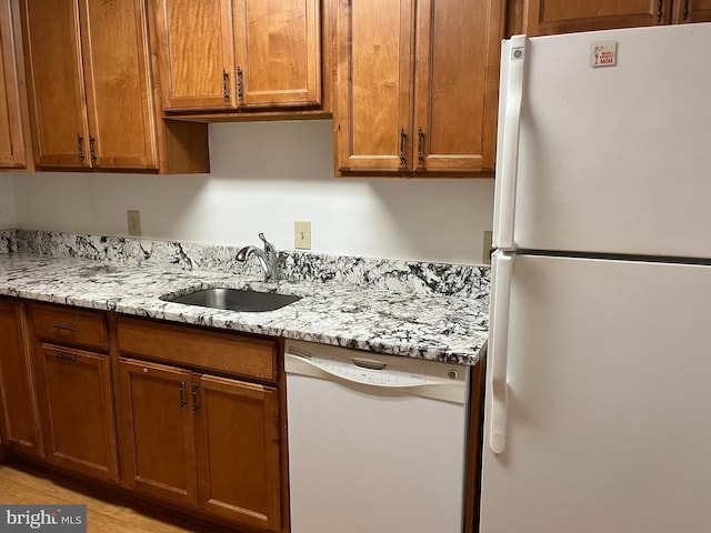 kitchen with white appliances, sink, light hardwood / wood-style flooring, and light stone counters