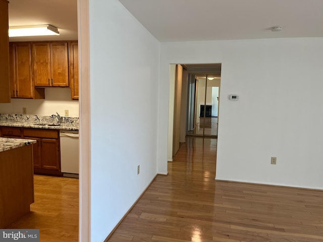 kitchen with light stone countertops, dishwasher, light hardwood / wood-style flooring, and sink