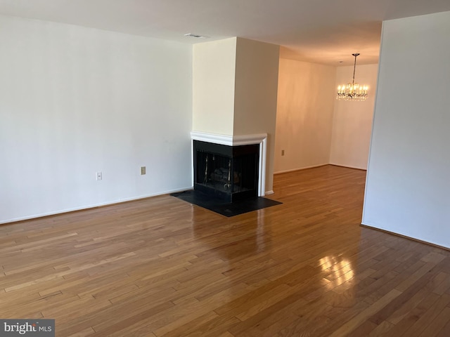 unfurnished living room with wood-type flooring, a multi sided fireplace, and a chandelier