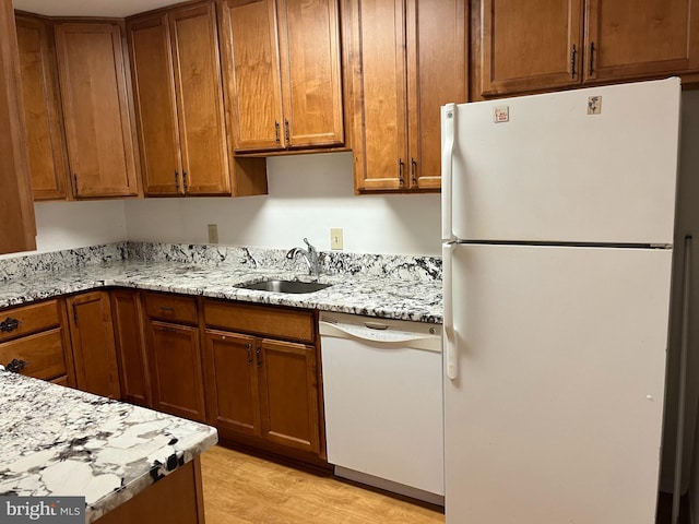 kitchen with light stone counters, light wood-type flooring, sink, and white appliances