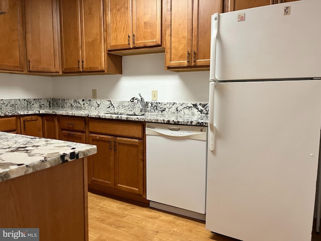 kitchen with light stone countertops, light hardwood / wood-style flooring, sink, and white appliances