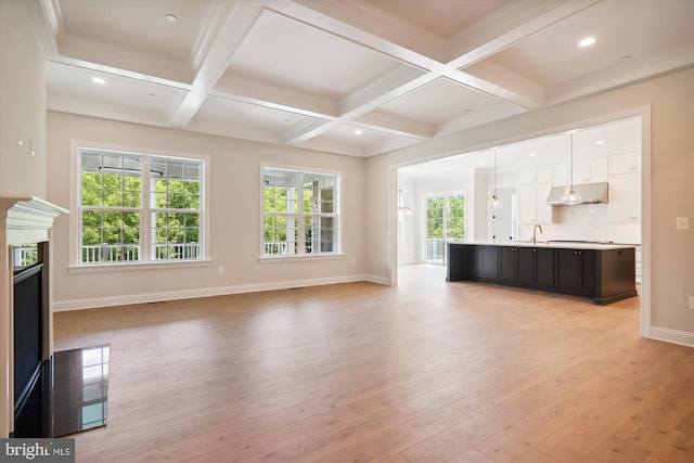 unfurnished living room with coffered ceiling, sink, light hardwood / wood-style floors, and beamed ceiling