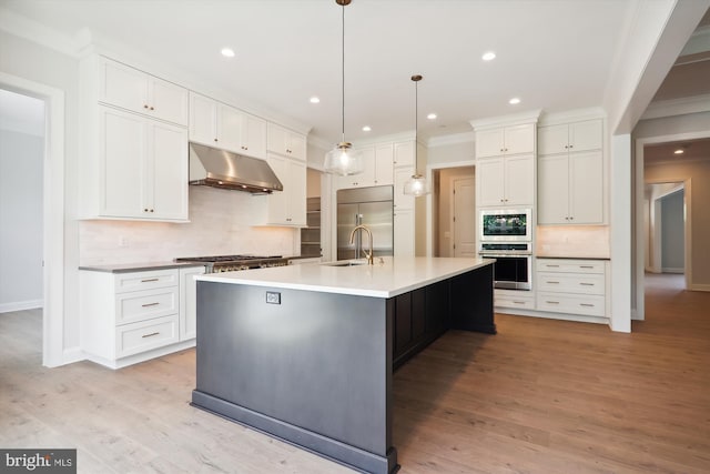 kitchen with built in appliances, light hardwood / wood-style flooring, pendant lighting, an island with sink, and white cabinetry