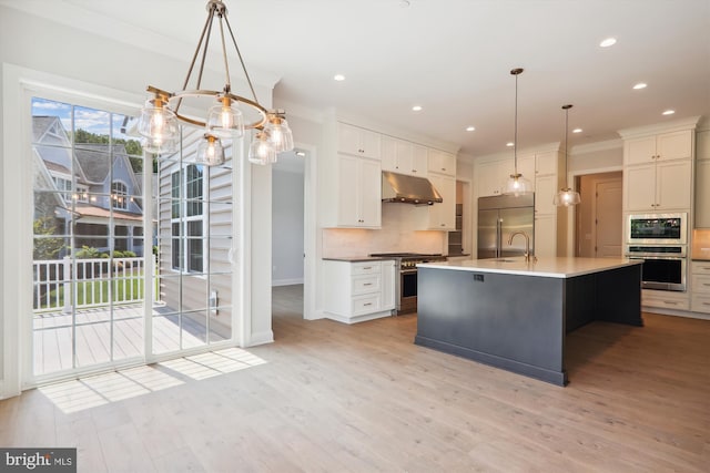 kitchen featuring built in appliances, pendant lighting, an island with sink, tasteful backsplash, and light wood-type flooring