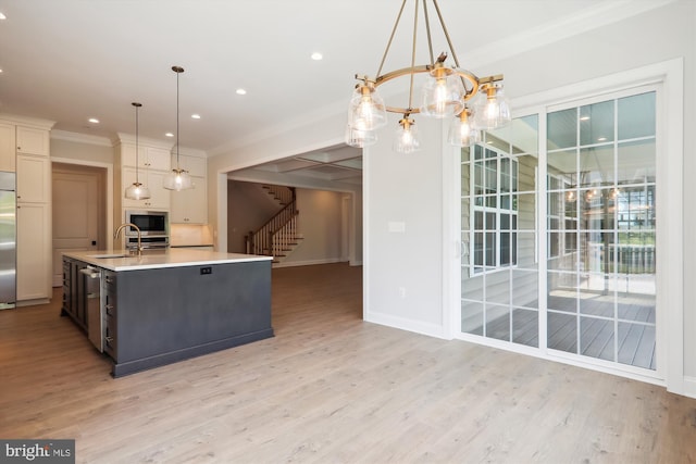 kitchen with sink, hanging light fixtures, an island with sink, and light wood-type flooring