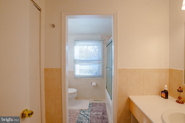 full bathroom with combined bath / shower with glass door, tile patterned floors, toilet, vanity, and tile walls