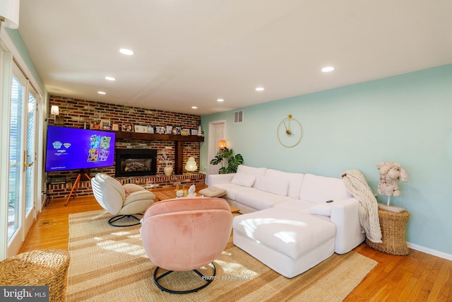 living room featuring a fireplace, light hardwood / wood-style floors, and brick wall