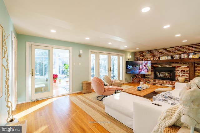 living room featuring a brick fireplace, french doors, brick wall, and light hardwood / wood-style flooring