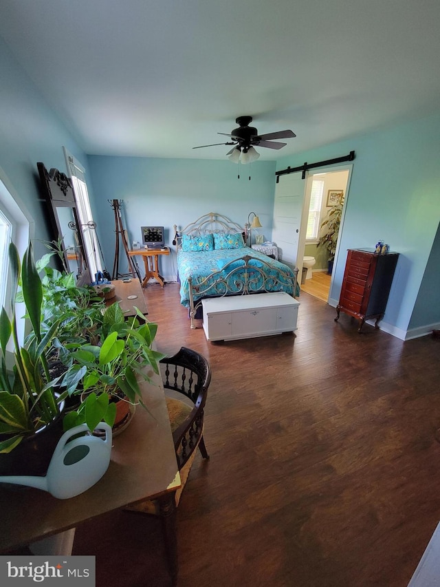 bedroom featuring ceiling fan, a barn door, dark hardwood / wood-style floors, and ensuite bathroom